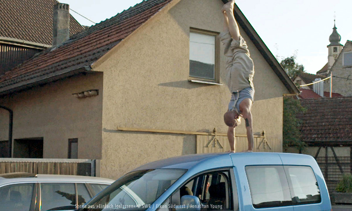 Bild eines Mannes der einen Handstand auf einem Autodach macht