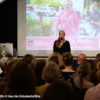 Bild von Frau mit Mikrofon vor einer Leinwand