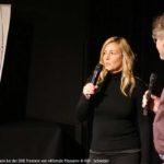 Frau und Mann mit Mikrofon vor einer Kinoleinwand