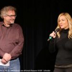 Frau und Mann mit Mikrofon vor einer Kinoleinwand
