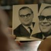 Person hält zwei schwarz/weiß Fotos eines Mannes