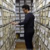 Mann steht zwischen zwei Regalen in einem Archiv