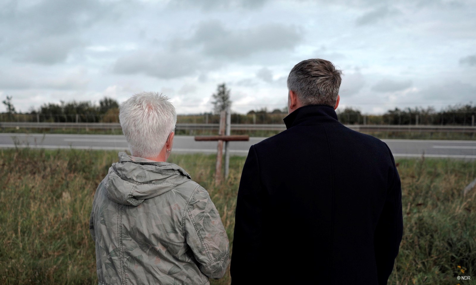 Filmstill aus "Der Sandsturm": Angehörige stehen vor dem Gedenkkreuz bei der Autobahn © NDR