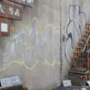 Loveparade – Die Verhandlung: Die Gedenkstätte für die Toten und Verletzten der Loveparade 2010 in Duisburg. Bild einer Wand mit Treppe auf der Kerzen und Graffiti zu sehen sind.