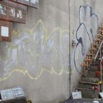 Loveparade – Die Verhandlung: Die Gedenkstätte für die Toten und Verletzten der Loveparade 2010 in Duisburg. Bild einer Wand mit Treppe auf der Kerzen und Graffiti zu sehen sind.