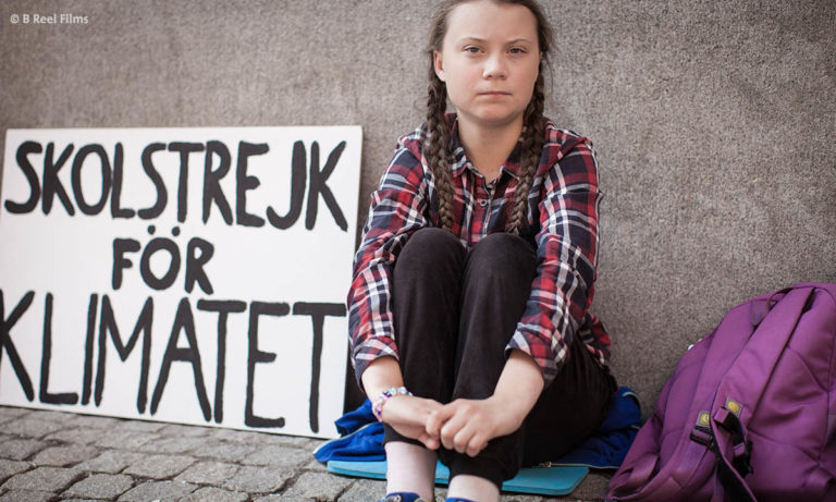 Greta Thunberg sitzt während ihres Schulstreiks vor einem Gebäude. (Foto: B-Reel Films)