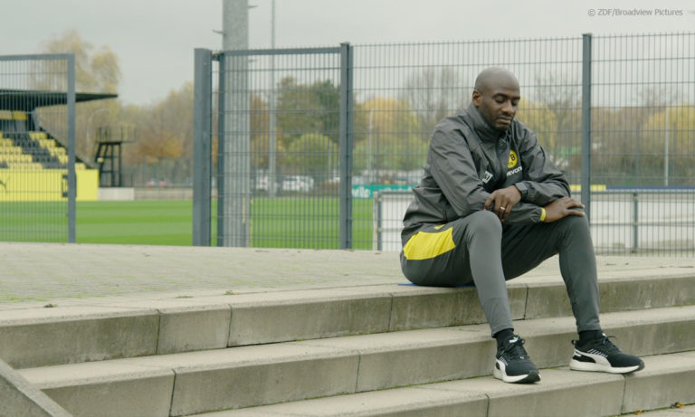 Filmstill aus "Schwarze Adler", zu sehen ist Ex-BVB-Profi Otto Addo in einer nachdenklichen Pose, während er auf einer Treppe sitzt © ZDF/Broadview Pictures