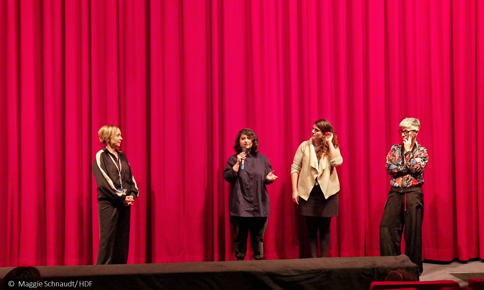 Frauen vor Kinovorhang v.l.n.r.: Moderatorin, Helin Celic, Rebeca Sánchez López und Raquel Fernández Núñez.