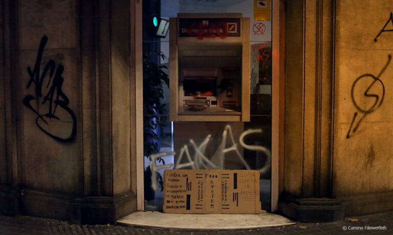 Filmstill aus ROBIN BANK. Zu sehen ist ein mutmaßlich kaputter Geldautomat, der mit antikapitalistischen Graffitis beschmiert ist © Camino Filmverleih