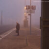 Filmstill aus DIE KINDER AUS KORNTAL. Man sieht einen Mann am S-Bahnhof Korntal. Dieser Bahnhof liegt im Nebel. Die Stimmung wirkt gedrückt. Der Mann schaut nach unten, sein Gesicht ist nicht zu sehen, er steht im seitlichen Profil. (Credit: DOK Leipzig 2023/DIE KINDER AUS KORNTAL, Regie: Julia Charakter)